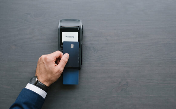 Man using contactless credit card terminal for digital payment at a wooden checkout counter in retail store