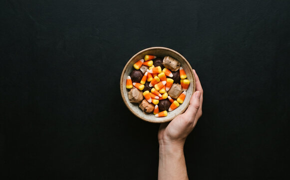 A person holding a bowl full of Halloween candy and candy corn on a dark background