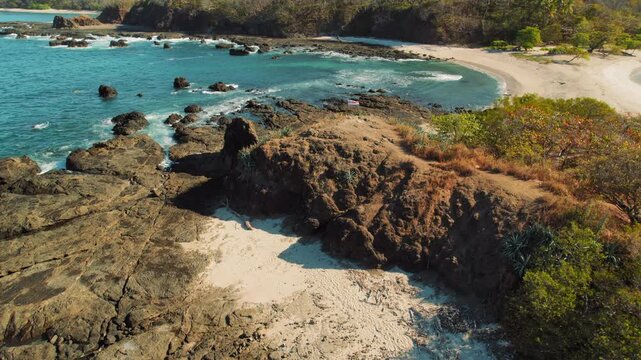 Flag on rocky coastline with turquoise ocean waves and sandy beach in Costa Rica