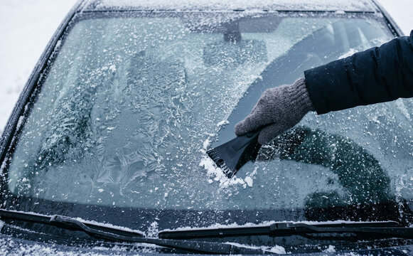 Person scraping frost and snow from a car windshield on a cold winter morning, vehicle maintenance concept
