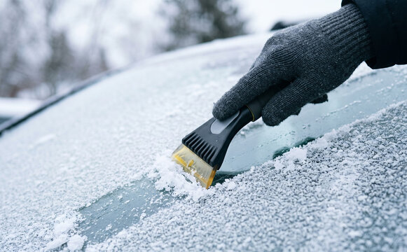 Person with glove scraping frost and ice from a car windshield on a cold winter morning, vehicle maintenance concept