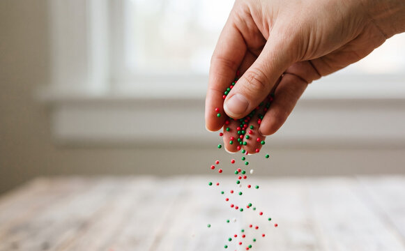 Close up of a woman hand scattering colorful sweet sprinkles for baking and holiday desserts