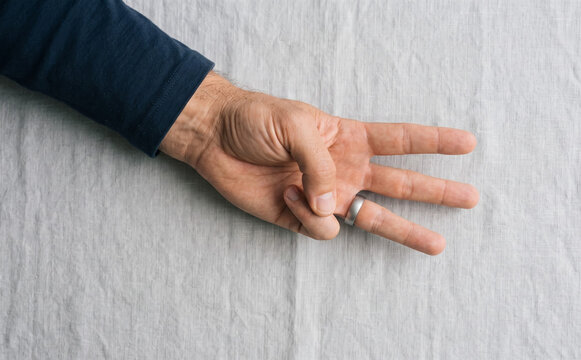 Adult male hand gesturing three fingers on textured linen table surface showing numerical sign