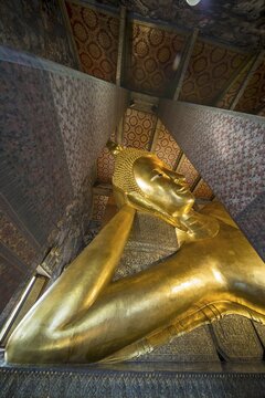 The monumental reclining Buddha shows the moment of entry into Nirvana. Golden surfaces, delicate patterns and warm temple colors accentuate the spiritual peace of this iconic depiction, Wat Pho, Bangkok, Thailand