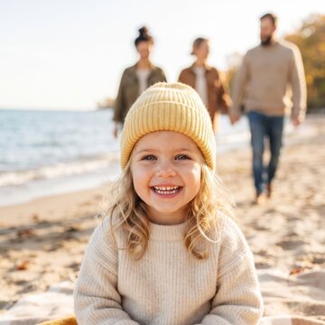 Happy little girl wearing a yellow beanie smiling on a beach with family in background