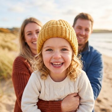 Happy family with young child in yellow beanie having fun on the beach at sunset