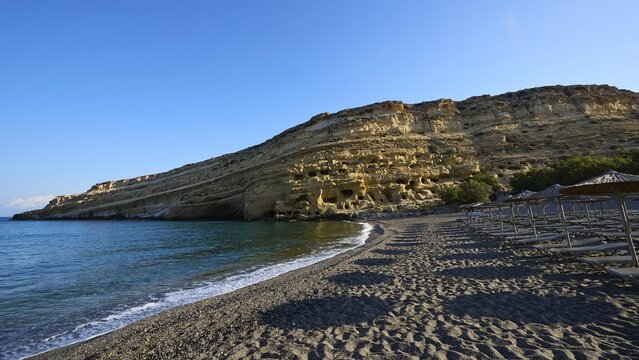 Neolithic caves, former hippie paradise, sandy beach with umbrellas and impressive rocks in front of calm sea, Matala, south coast, Crete, Greek Islands, Greece