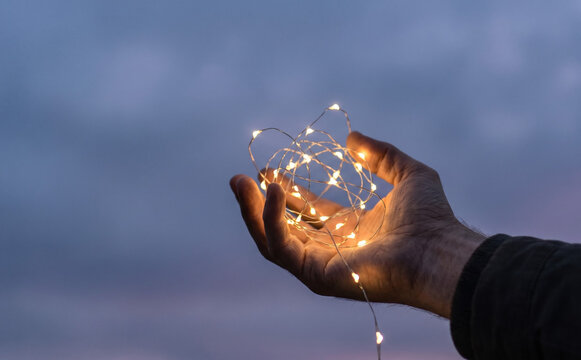 Man holding glowing string lights in hands representing creativity, magic, and imagination