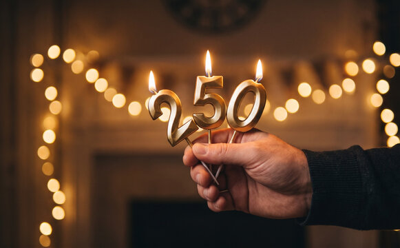 Person holding gold 250 candles with lit flames for a birthday celebration or milestone anniversary