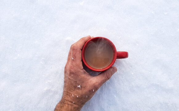 A male hand holding a hot red coffee mug in the snow during winter vacation