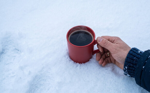 A person holding a red mug of hot coffee in the snow representing cozy winter warmth and outdoor relaxation