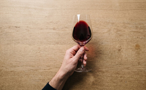 Hand holding a wine glass with red wine on wooden background top view