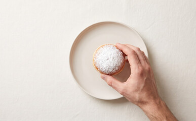 Naklejka premium Hand holding a sweet powdered donut on a white plate representing delicious bakery and dessert concepts