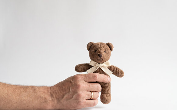 Man holding a small knitted brown teddy bear toy with a white ribbon on a white background