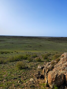 Scenic view of a vast green steppe with rocky hills under blue sky
