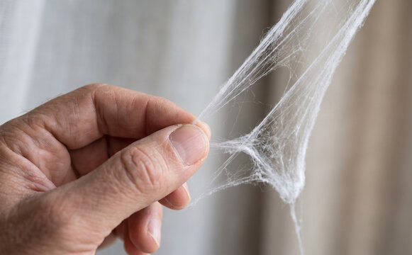 A mature man holding synthetic spider web stretching between his fingers for halloween decoration