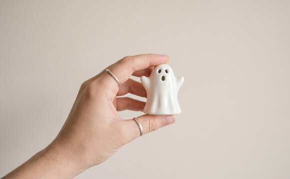 A person holding a small white ceramic ghost figurine in hand, minimalist Halloween decor and spooky spooky concept