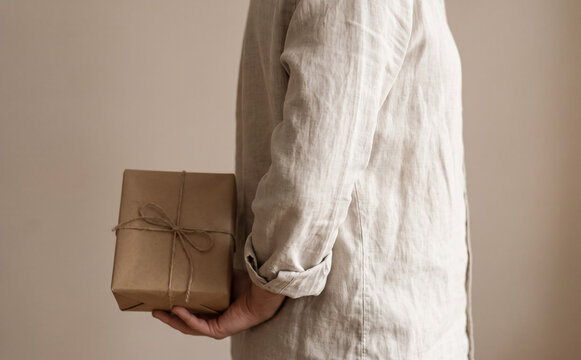 Woman holding a wrapped gift box behind her back wearing linen shirt surprise present for celebration