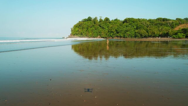 Wide aerial view of woman walking on wet sand beach in Costa Rica jungle