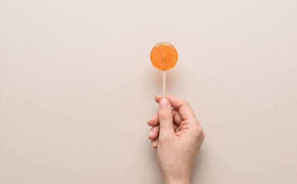 Hand holding an orange lollipop on a neutral background concept for sweet treats and candy