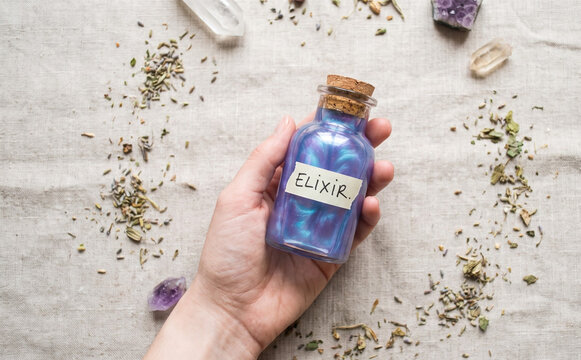 Magical purple elixir potion bottle held in hand with herbs and crystals for fantasy witchcraft and wellness