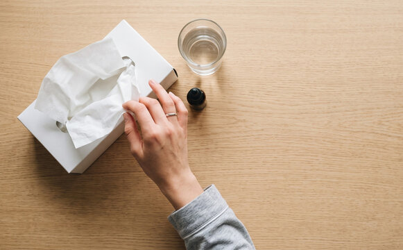 Woman pulling a tissue from a white box on a wooden table with water and oil