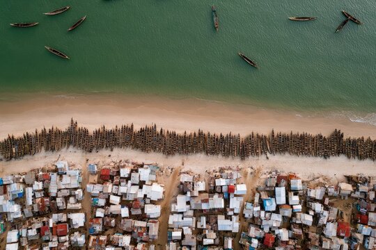 Aerial view of a coastal village, canoes on water, and a beach lined with structures