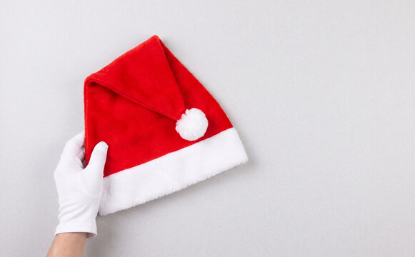 A person wearing white gloves holding a red Santa hat on a grey background for Christmas