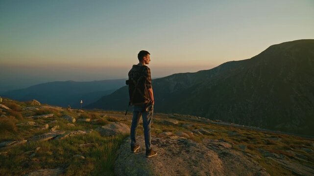 Person stands on a rock looking at mountain landscape during sunset in a natural setting surrounded by hills and open sky