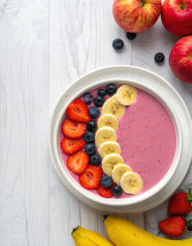 Berry smoothie bowl with banana, strawberry, blueberry, and apple on white wooden table