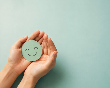 Cupped hands holding green smiley face icon for mental health and customer satisfaction