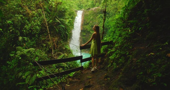Female tourist in dress admires la Pintada Blue Falls waterfall in Costa Rica rainforest
