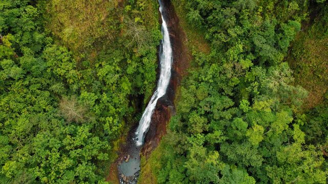 Aerial view of a long waterfall cutting through dense forest in Costa Rica
