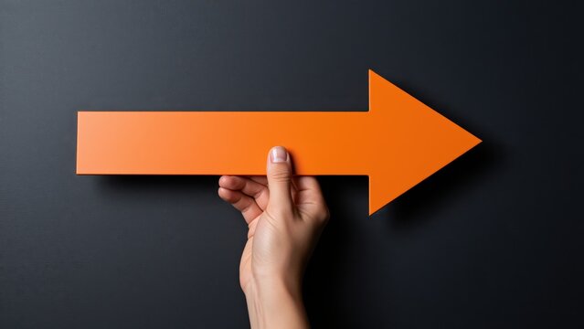 Hand Holding an Orange Arrow Sign Pointing to the Right on Dark Background for Business and Directional Concept