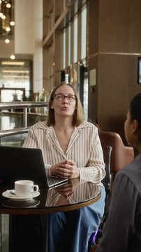 Vertical shot of Caucasian woman with disability talking and shaking hands with colleague at cafe table. Perfect for corporate diversity and inclusive employment campaigns