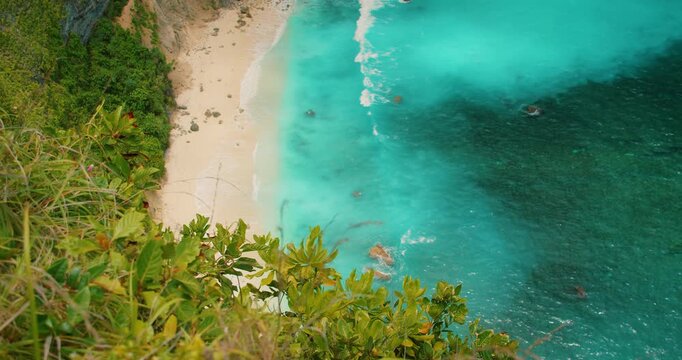 Bird eye view of turquoise sea waves crashing on sand at Kelingking Beach Bali