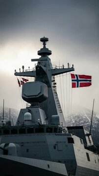 Norwegian naval warship frigate superstructure mast and flag sailing in Arctic waters with snowy mountains