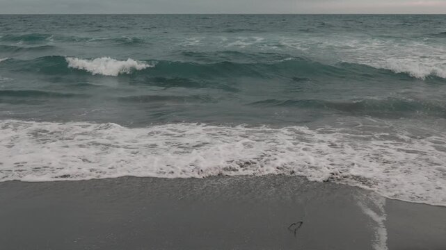 Intermittent waves breaking on a gray sandy beach beneath a gray sky

