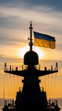 Silhouette of a Ukrainian naval warship mast with a national flag flying proudly against a golden sunset sky at sea, representing patriotism and defense