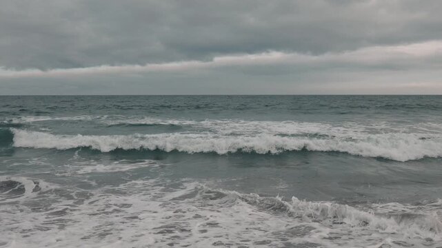 Intermittent waves breaking on a gray sandy beach beneath a gray sky
