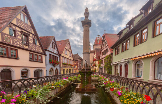 Stone fountain surrounded by traditional half-timbered houses and colorful flowers in Rothenburg ob der Tauber, Germany.