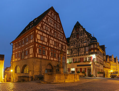 Traditional half-timbered architecture and a stone fountain illuminated at dusk in Rothenburg ob der Tauber, Germany.