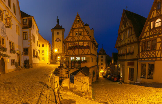 Half-timbered houses and cobblestone streets illuminated by warm streetlights during blue hour in Rothenburg ob der Tauber, Germany.