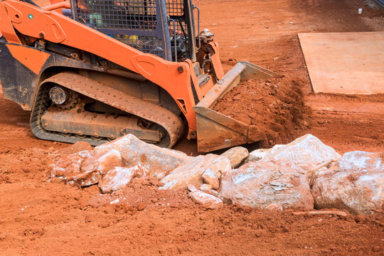 Small bulldozer is pushing dirt, rocks on construction site.