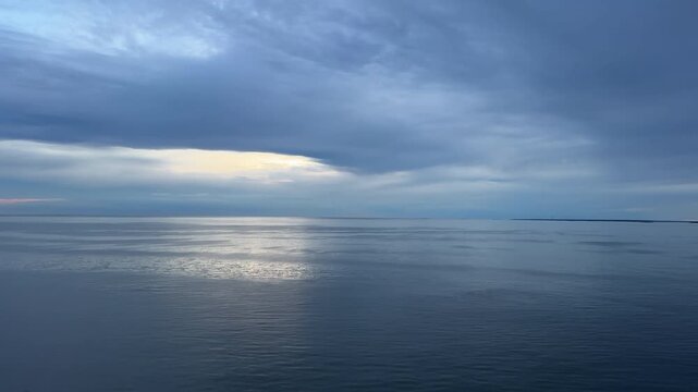 Wide seascape showing sunlight breaking through moody storm clouds and casting a bright silver reflection across the calm open waters of the Baltic Sea in Sweden.
