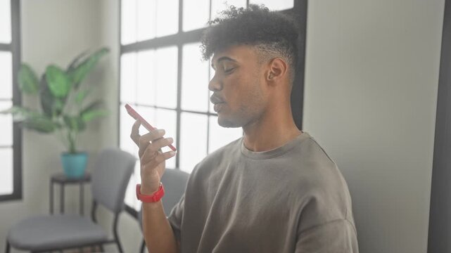 Man sitting in chair holding smartphone, hand raised to screen, waiting in a building; calm patience.