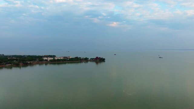 Hefei Chaohu Zhongmiao Aerial: Ancient Temple on Shore Reflects in Blue Waves with Distant Boats Under Cloudy Sky