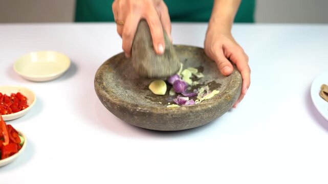 Female hands crushing garlic and shallots using traditional stone mortar and pestle for cooking