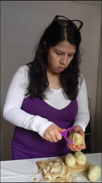 Pregnant woman peeling potatoes with a purple peeler in kitchen