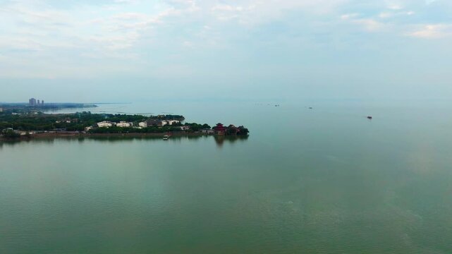 Hefei Chaohu Zhongmiao Aerial: Ancient Temple on Shore Reflects in Blue Waves with Distant Boats Under Cloudy Sky